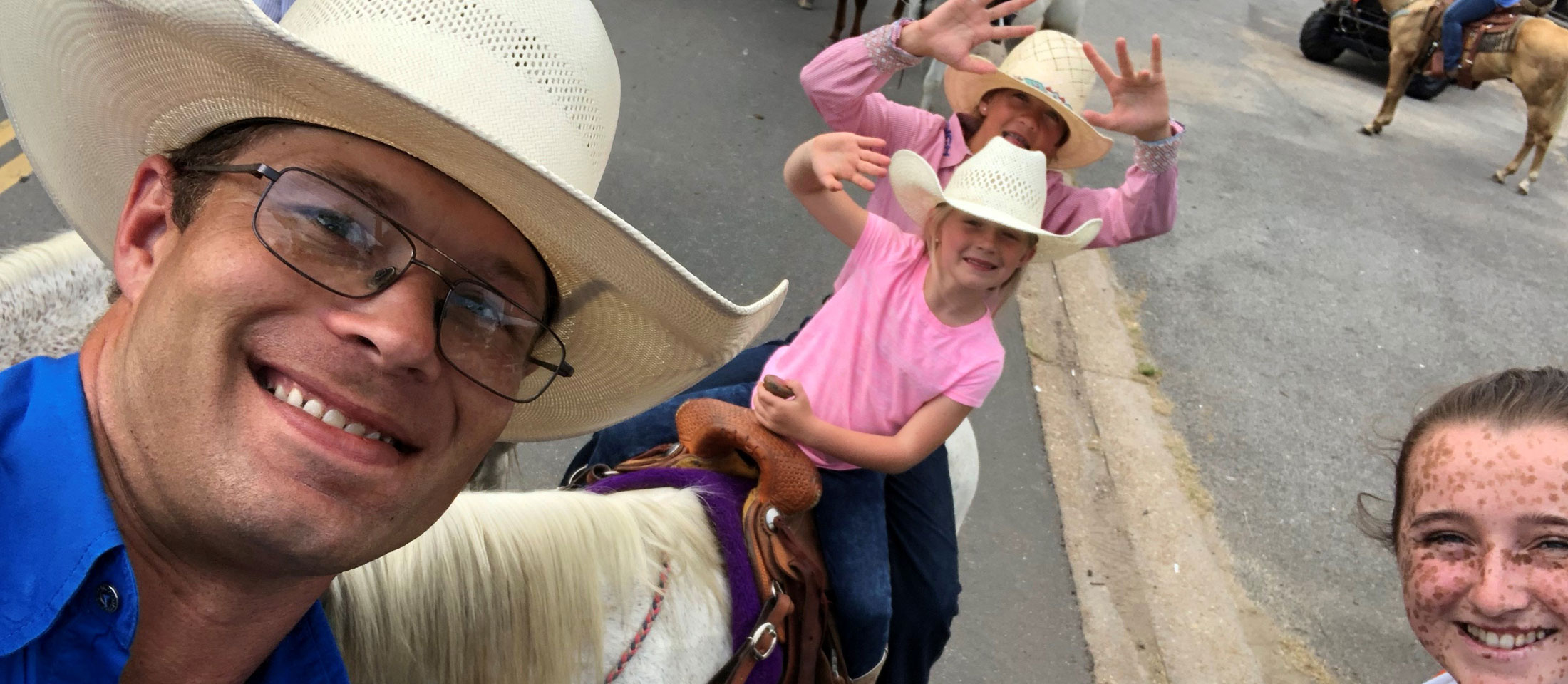 A cowboy taking a picture with two girls on a pony and another girl smiling.